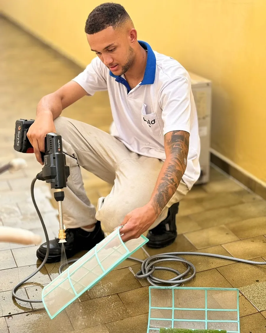Técnico da Cold&Ice com a furadeira e o filtro de um ar condicionado nas mãos